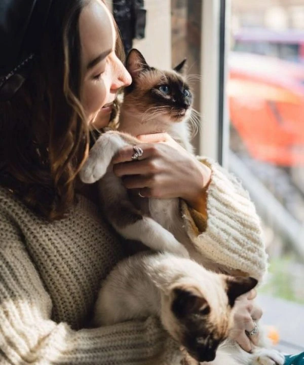 chica con gato siamese a la ventana